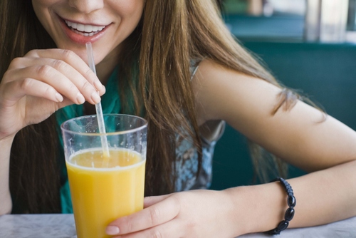 Woman drinking orange juice from a straw.
