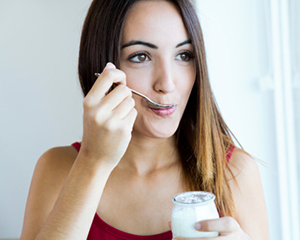 Smiling woman eating yogurt after her oral surgery.