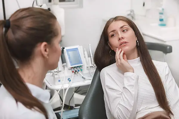 A woman touching her jaw while discussing TMD/TMJ pain and treatment options, such as Botox, with a specialist.
