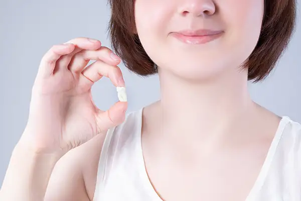 A woman smiling while holding an extracted tooth between her fingers, demonstrating post-extraction care.